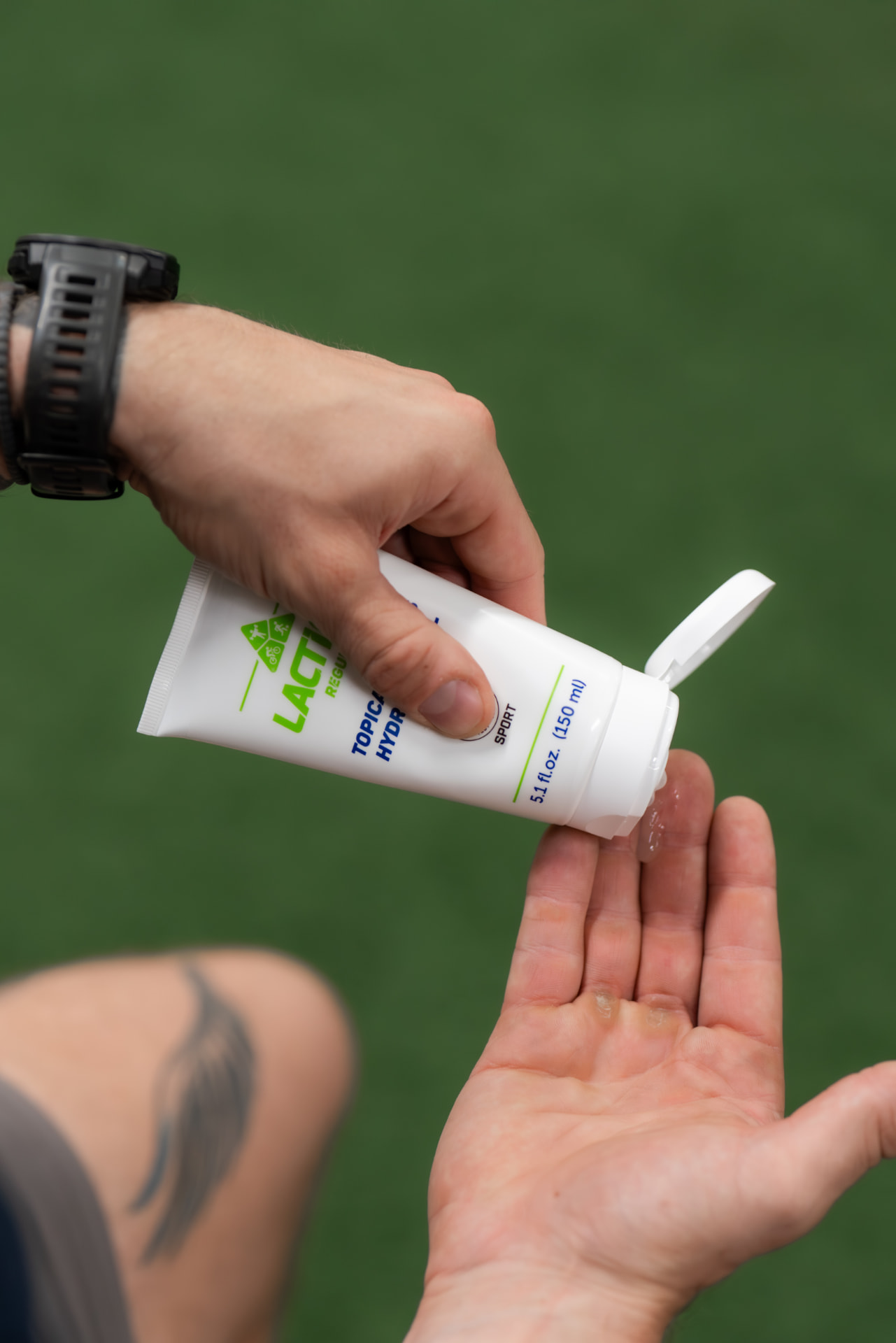 A person dispensing LactiGo gel from the tube into their hand beside a sports field