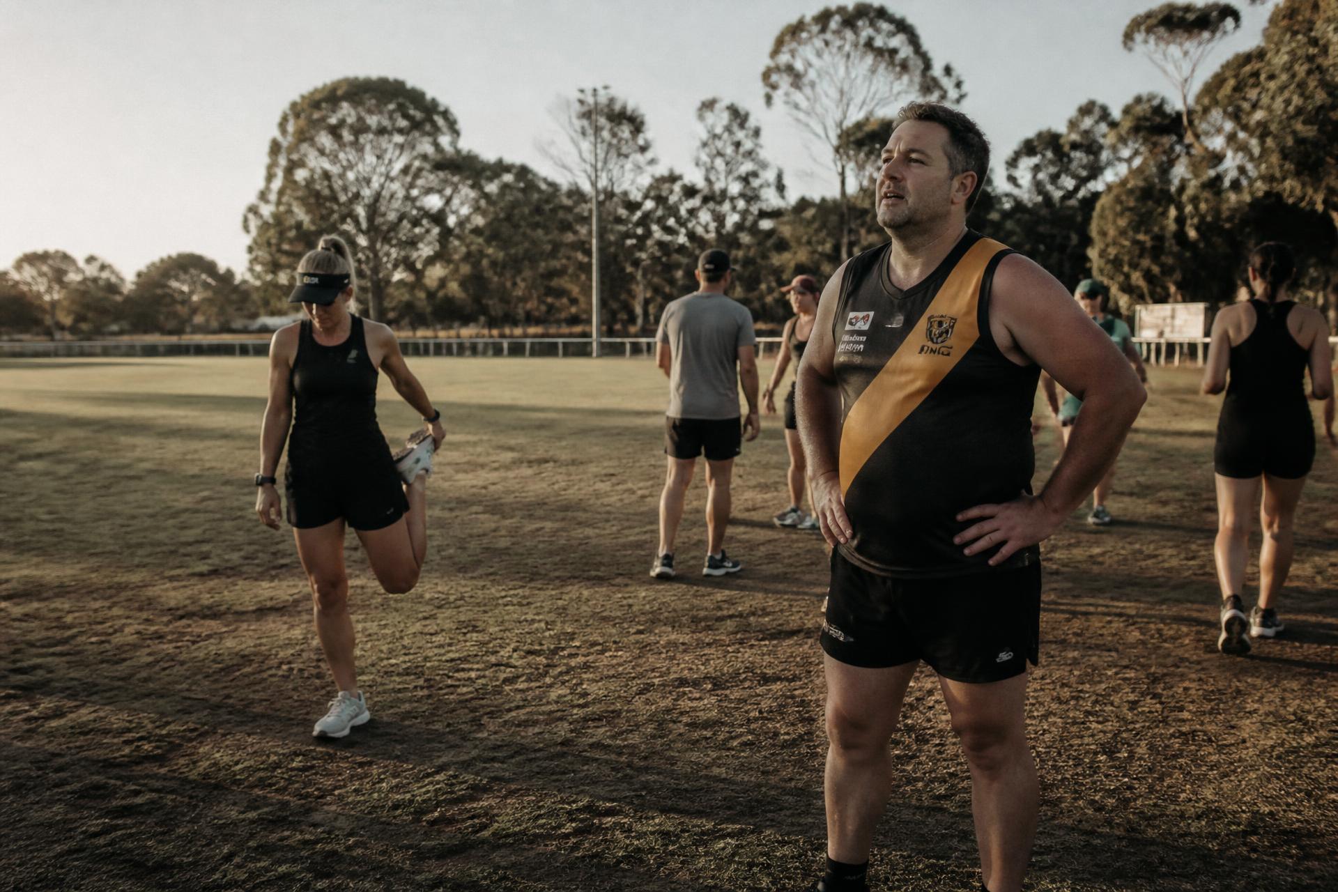 Community football players and runners cooling down on an Australian suburban oval at sunrise