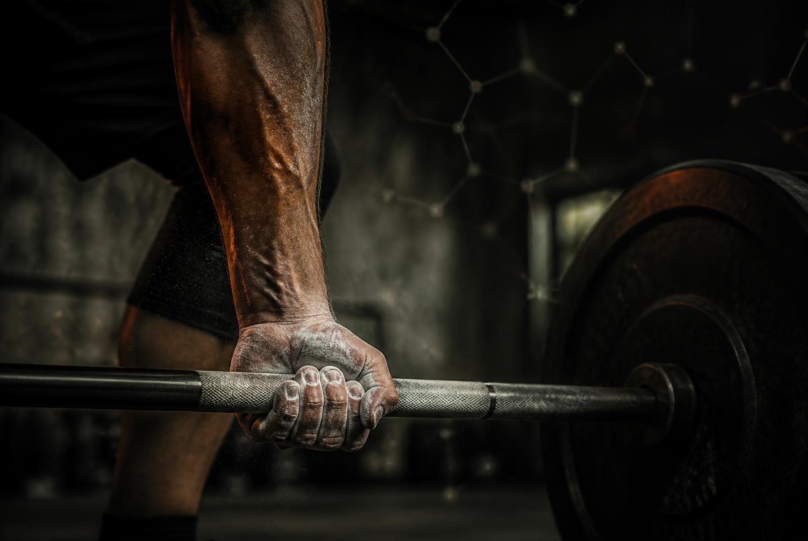 Chalked hand gripping a barbell in a dark concrete gym, with a faint molecular lattice of light in the background
